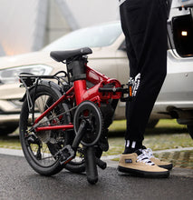 Load image into Gallery viewer, A lifestyle image of a Dahon Unio E20 folding electric bike with the frame colour red. The bike is folded next to the boot of a car.