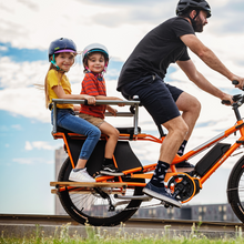 Load image into Gallery viewer, A photo of the Yuba Kombi E5 electric longtail cargo bike with two child passengers on the back. The bike is accessorised with the Yuba Kombi Family Pack.