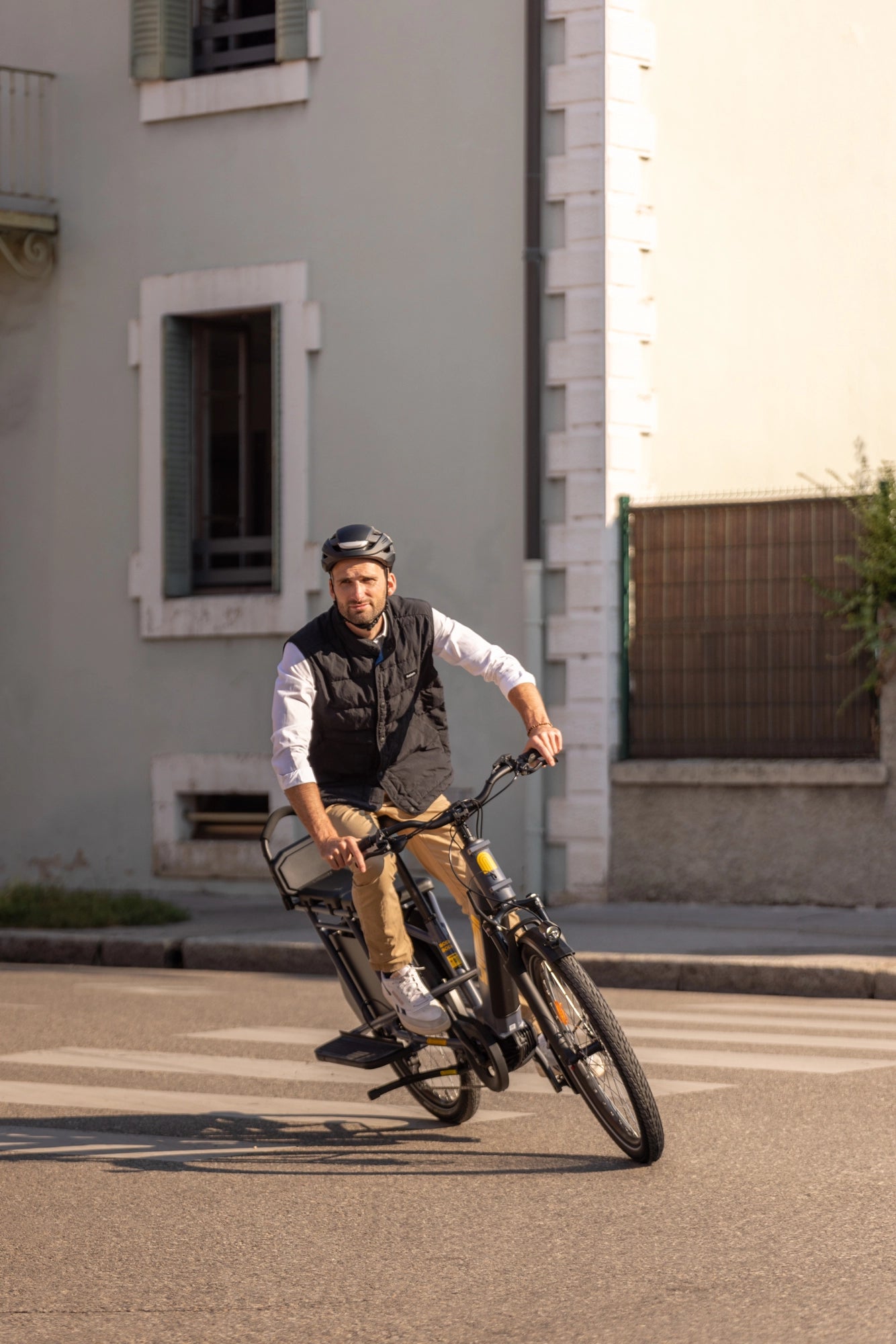 A lifestyle image of a man cycling a Yuba Boda Boda electric longtail cargo bike in an urban setting.