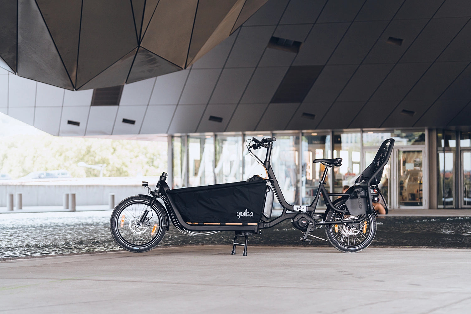 A lifestyle image of the Yuba Open Loader cargo box setup for the Yuba Supercargo CL electric cargo bike, shown in an urban setting.