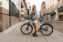 Load image into Gallery viewer, A lifestyle image of the BESV CT 2.2 LS electric bike taken on an urban street with a female model.