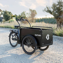 Load image into Gallery viewer, Lifestyle image of the Bimas eCargo 3.3 Premium electric cargo bike, shown in a rural setting on a gravel road on a sunny evening.