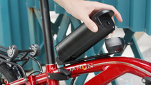 Load image into Gallery viewer, Person attaching a black battery pack to a red Dahon bicycle with a blue background
