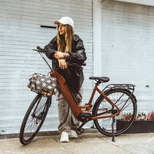 Load image into Gallery viewer, A lifestyle image of the Kuma S1 electric bike featuring a woman wearing streetwear standing on a street next to a Kuma S1 bike.
