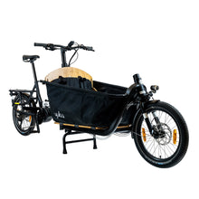 Load image into Gallery viewer, A product image of the Yuba Supercargo CL electric front-loading cargo bike. The model shown has a black frame, a canvas box with child seats at the front. The bike is available to buy from Bleeper.
