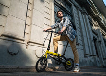 Load image into Gallery viewer, Man with a yellow and black bicycle in front of a building