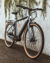 Load image into Gallery viewer, A lifetstyle image of the Kuma M1 electric bike with the bike parked against a white wall.
