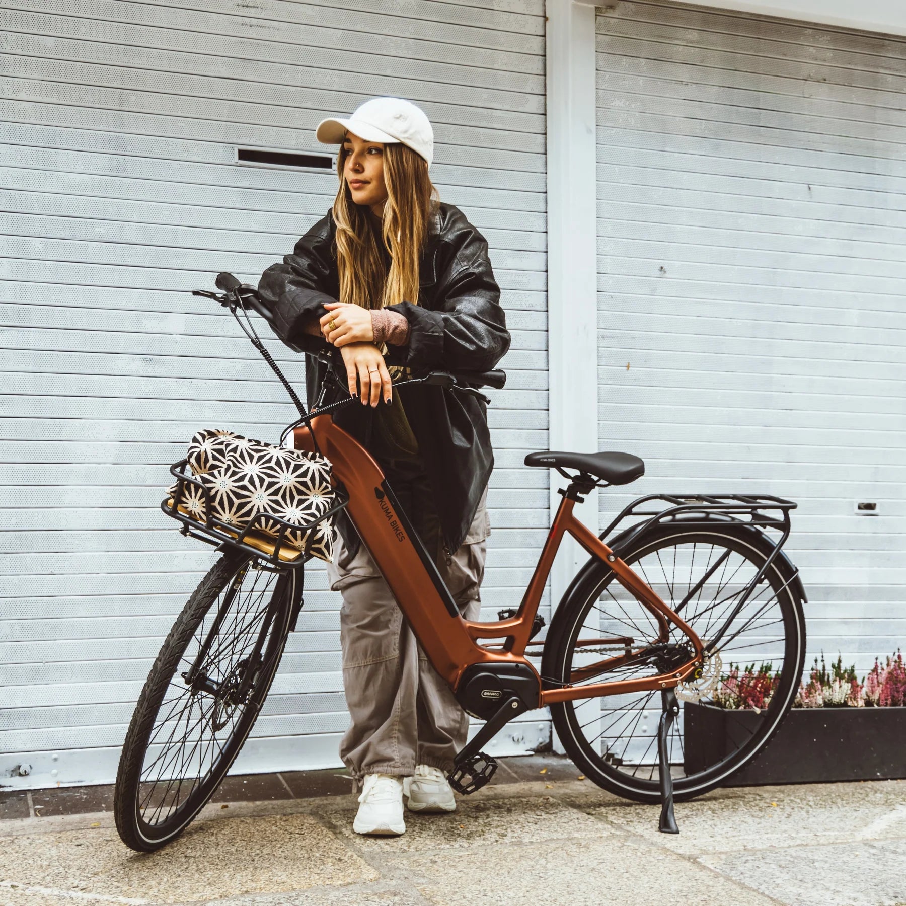 A lifestyle image of the Kuma S1 electric bike featuring a woman wearing streetwear standing on a street next to a Kuma S1 bike.