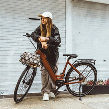 Load image into Gallery viewer, A lifestyle image of the Kuma S1 electric bike featuring a woman wearing streetwear standing on a street next to a Kuma S1 bike.
