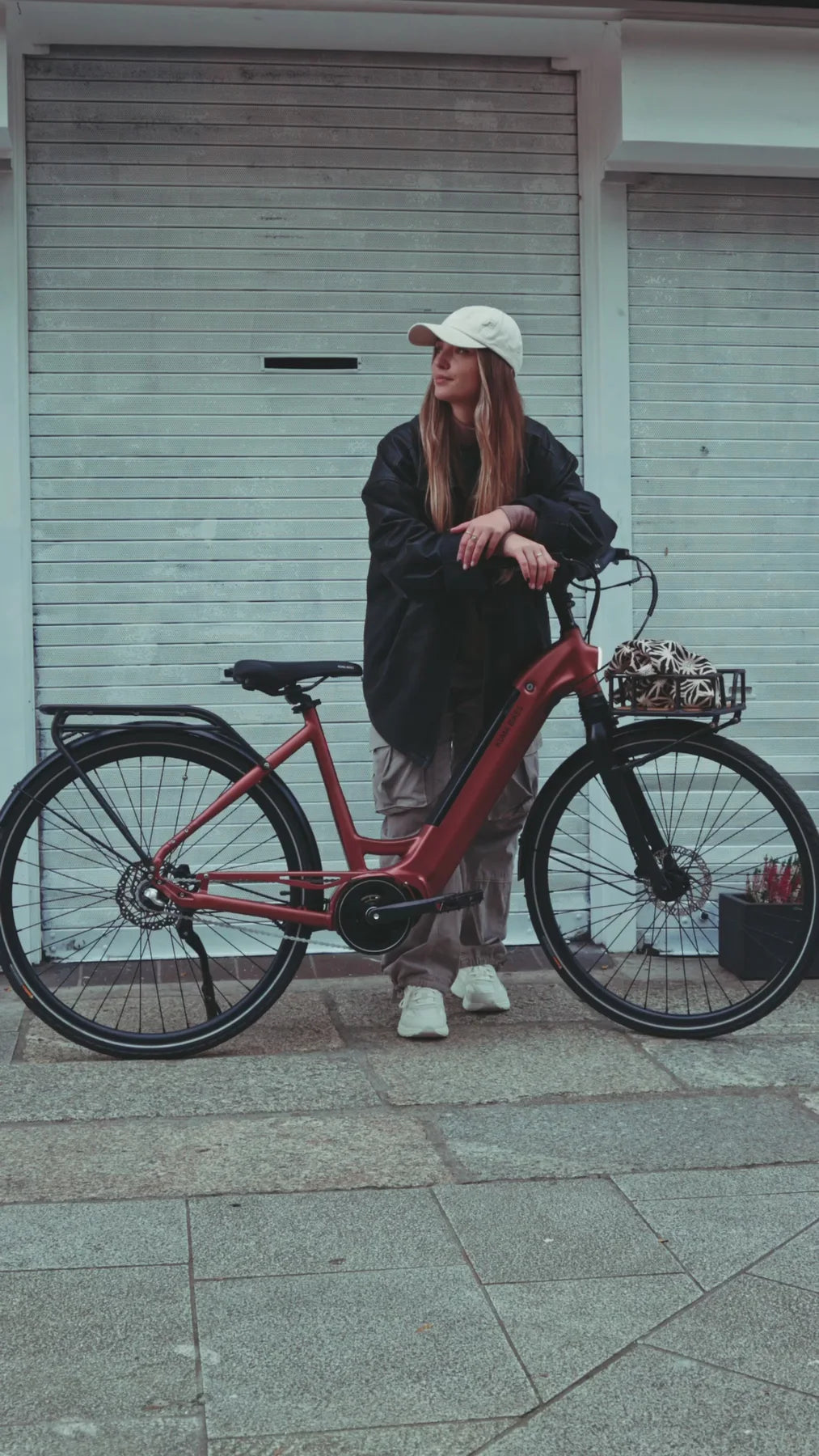 A lifestyle image of the Kuma S1 electric bike featuring a woman wearing streetwear standing on a street next to a Kuma S1 bike.