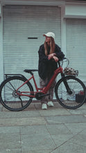 Load image into Gallery viewer, A lifestyle image of the Kuma S1 electric bike featuring a woman wearing streetwear standing on a street next to a Kuma S1 bike.
