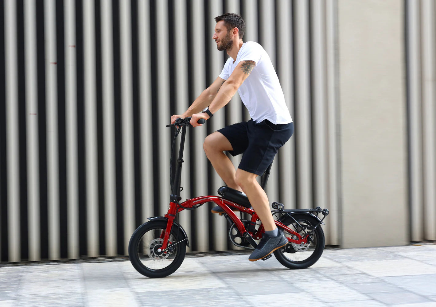 A lifestyle image showing the Dahon Curl Ei4 electric folding bike being cycled by a man in an urban setting. The frame colour is red.