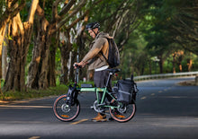 Load image into Gallery viewer, A man in a cycle helmet walking beside a green Dahon folding electric bike on a tree-lined road

