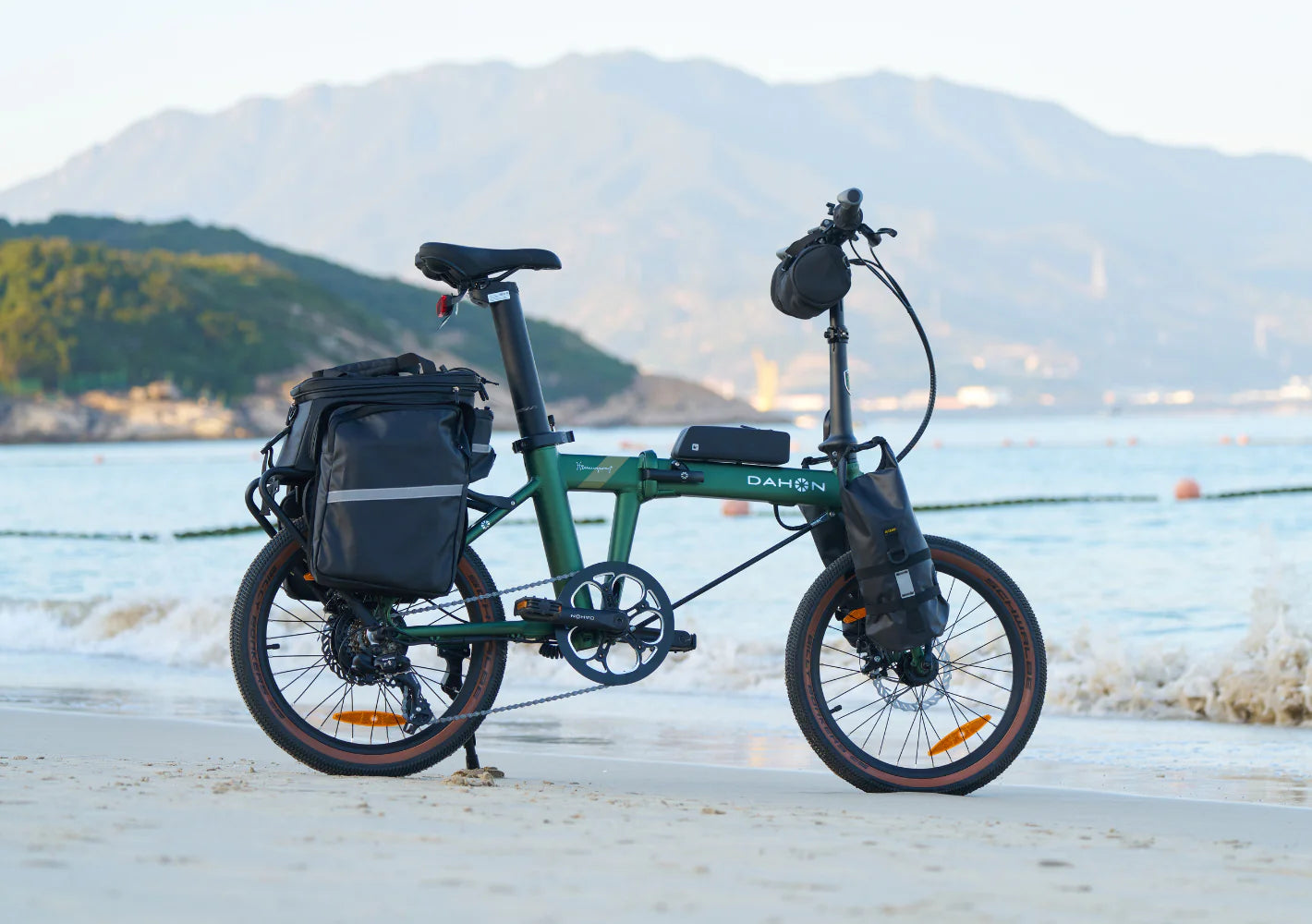 Green Dahon folding electric bike on a beach with mountains in the background