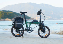 Load image into Gallery viewer, Green Dahon folding electric bike on a beach with mountains in the background
