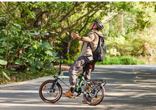 Load image into Gallery viewer, Person riding a bicycle on a road with greenery in the background
