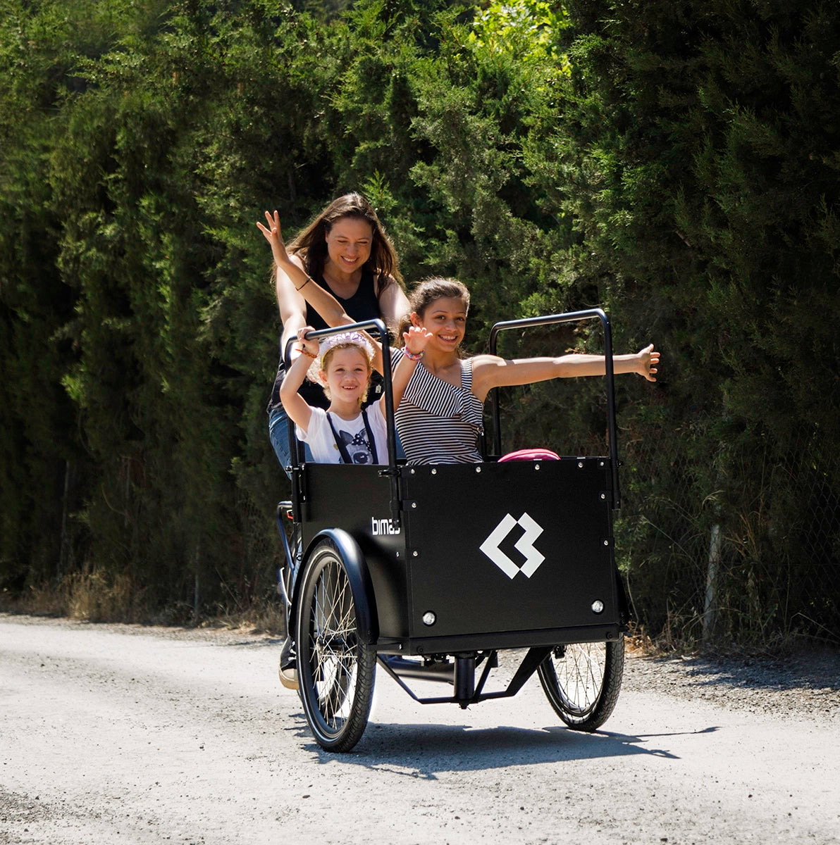 A photo of a woman cycling two girls in a Bimas ecargo electric cargo bike. 