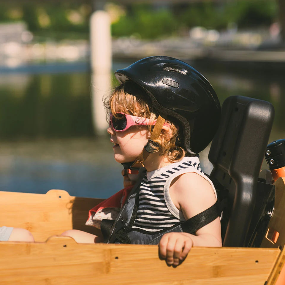 A lifestyle image showing the Yuba 2be3 child seat inside the Bamboo Box of the Yuba Supercargo CL electric cargo bike with a child passenger strapped into the seat.