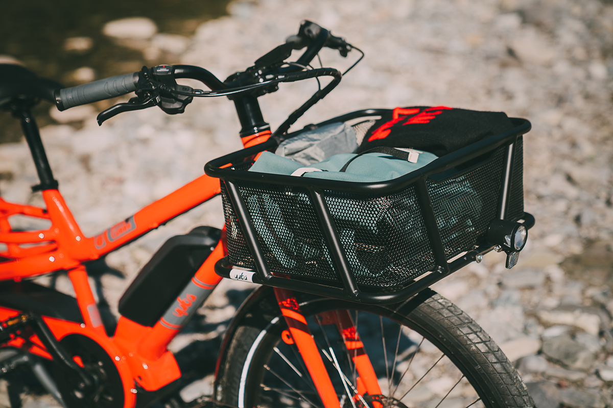 A product image of the Yuba Bread Basket accessory attached to the front of a Yuba Spicy Curry electric longtail cargo bike.