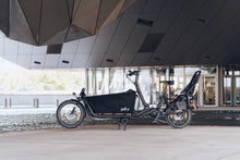 Load image into Gallery viewer, A lifestyle image of the Yuba Open Loader cargo box setup for the Yuba Supercargo CL electric cargo bike, shown in an urban setting.
