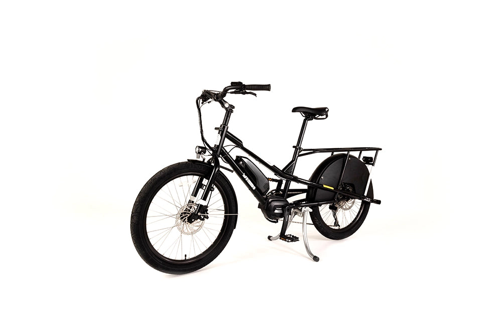 A product image of the Yuba Kombi E6 electric longtail cargo bike taken at an oblique angle from the front left of the bike. This is the bare layout of the bike, with no accessories added. The bike has a black frame. 