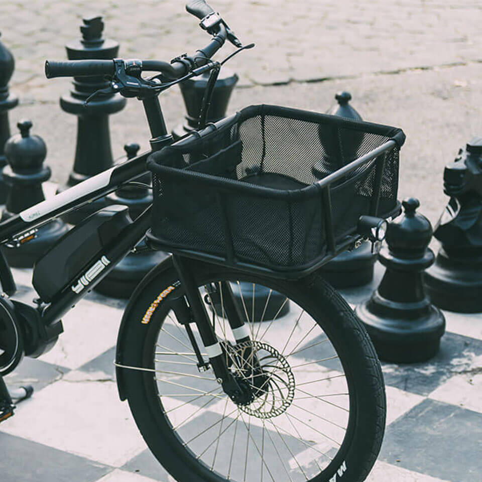 A photo of a Yuba Stuff Rack front basket attached to a Yuba longtail cargo bike, pictured in an urban park beside a giant chess board. 