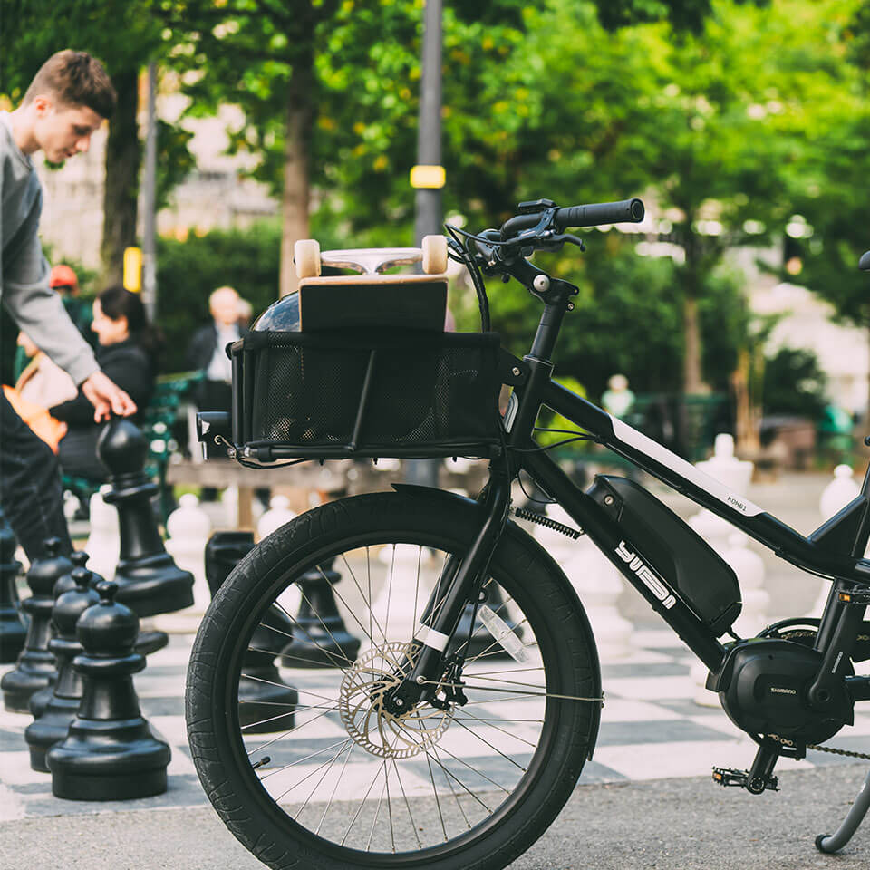 A photo of a Yuba Stuff Rack front basket attached to a Yuba longtail cargo bike, pictured in a urban park, with a skate board and skate helmet stored in the basket.