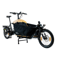 Load image into Gallery viewer, A product image of the Yuba Supercargo CL electric front-loading cargo bike. The model shown has a black frame, a canvas box with child seats at the front. The bike is available to buy from Bleeper.
