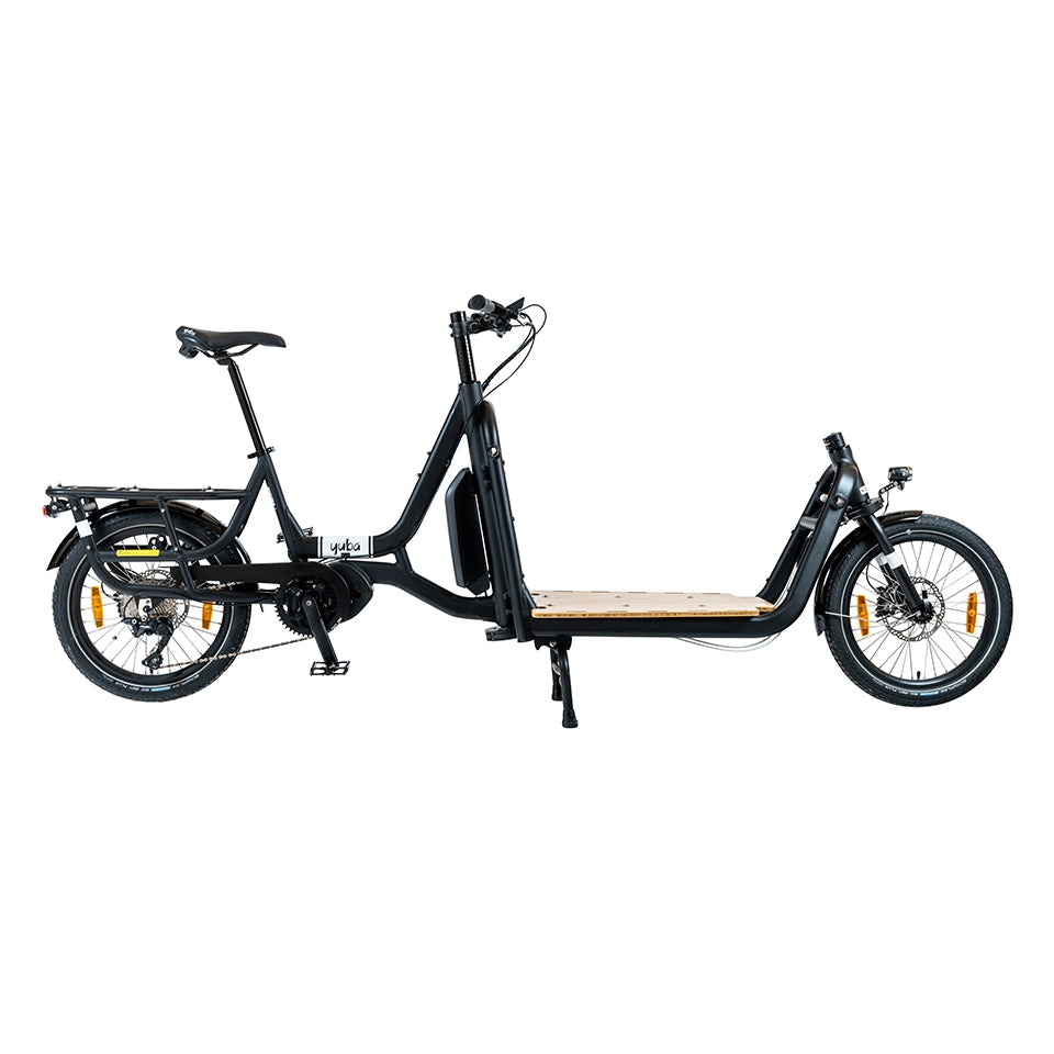 A product image of the Yuba Supercargo CL electric front-loading cargo bike. The model shown has a black frame and a simple timber flatbed on the front end. The bike is available to buy from Bleeper.