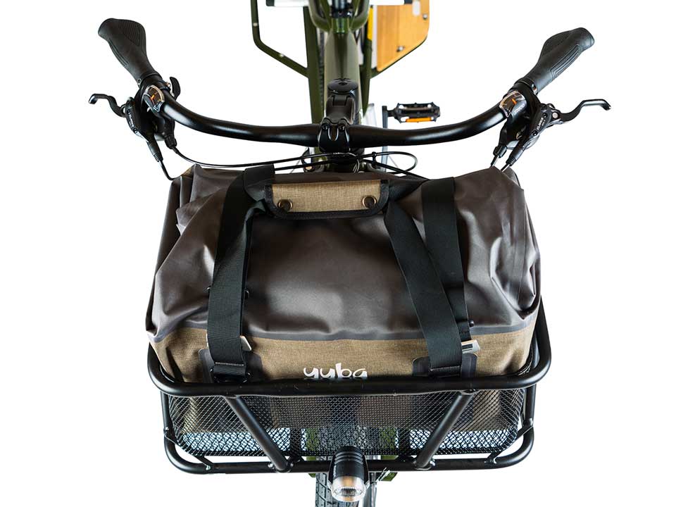 A product image for the Yuba Grab and Go bag sitting in the front basket of a Yuba longtail cargo bike. The photo is taken from the top down.