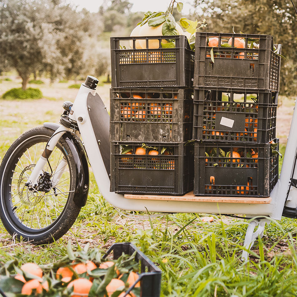 A product image of the Yuba Supercargo bamboo base board, which attaches to the Yuba Supercargo CL electric cargo bike. In the photo there are six plastic crates filled with fruit loaded onto the Bamboo baseboard.