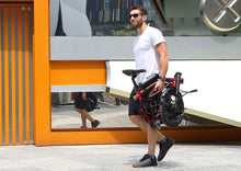 Load image into Gallery viewer, Man carrying a Dahon Curl folded electric bike in an urban setting
