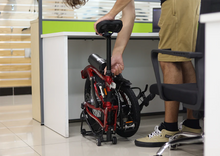 Load image into Gallery viewer, The Dahon Curl shown in its folded configuration under a desk.
