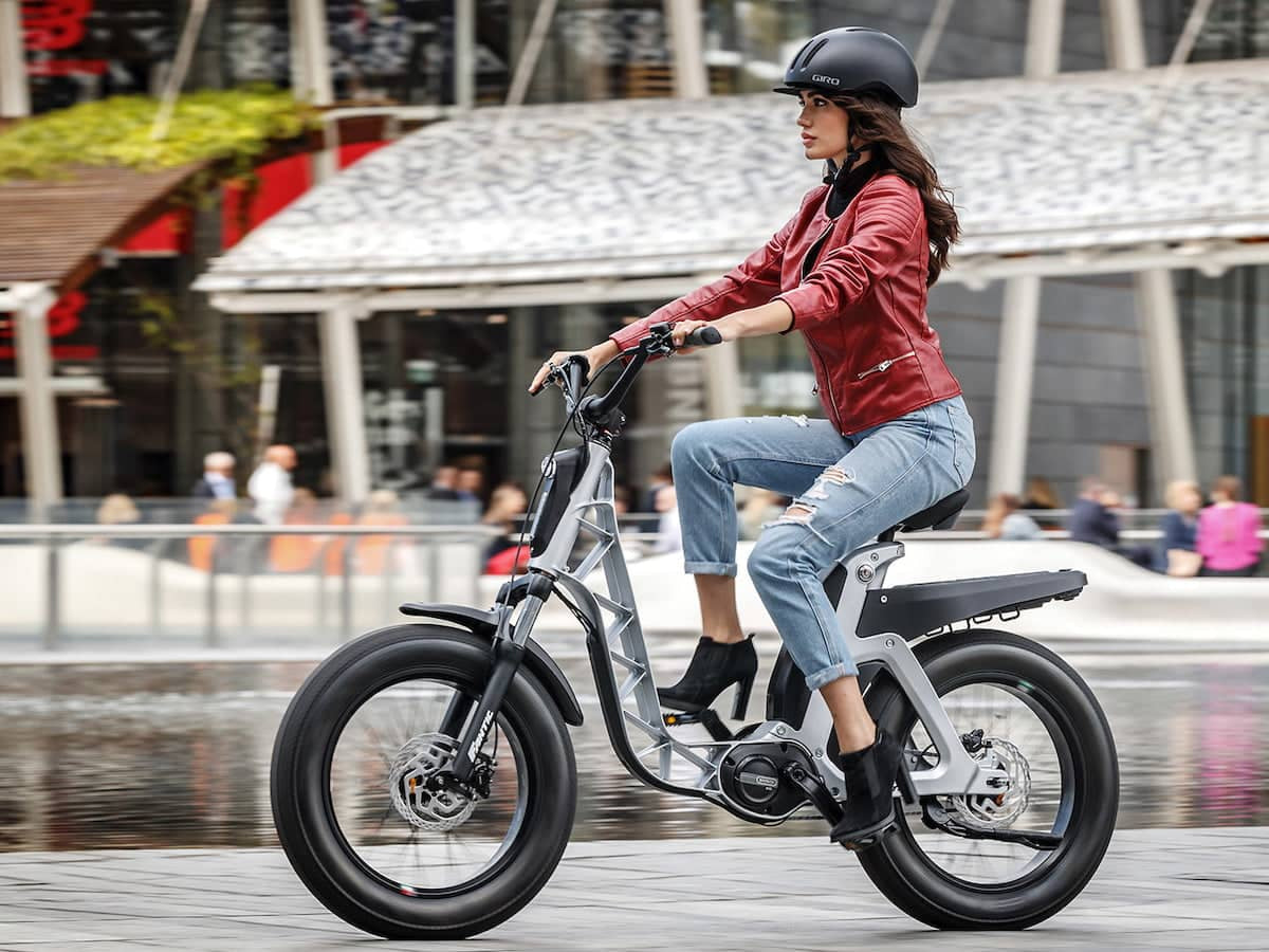 A lifestyle image of the Fantic Issimo Urban electric bike, with a woman sitting on the bike in an urban setting.