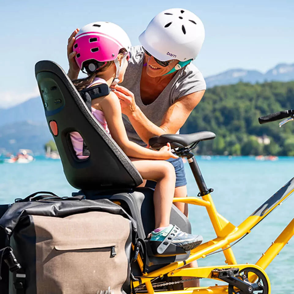 An image showing the Thule Yepp Nexxt 2 Maxi child seat installed on the rear of a Yuba longtail cargo bike. A woman is securing her child into the seat. 